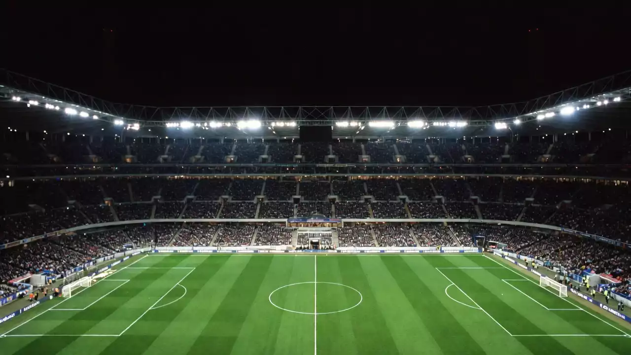 Aficionados viendo un partido de fútbol nocturno en un estadio lleno con el césped iluminado